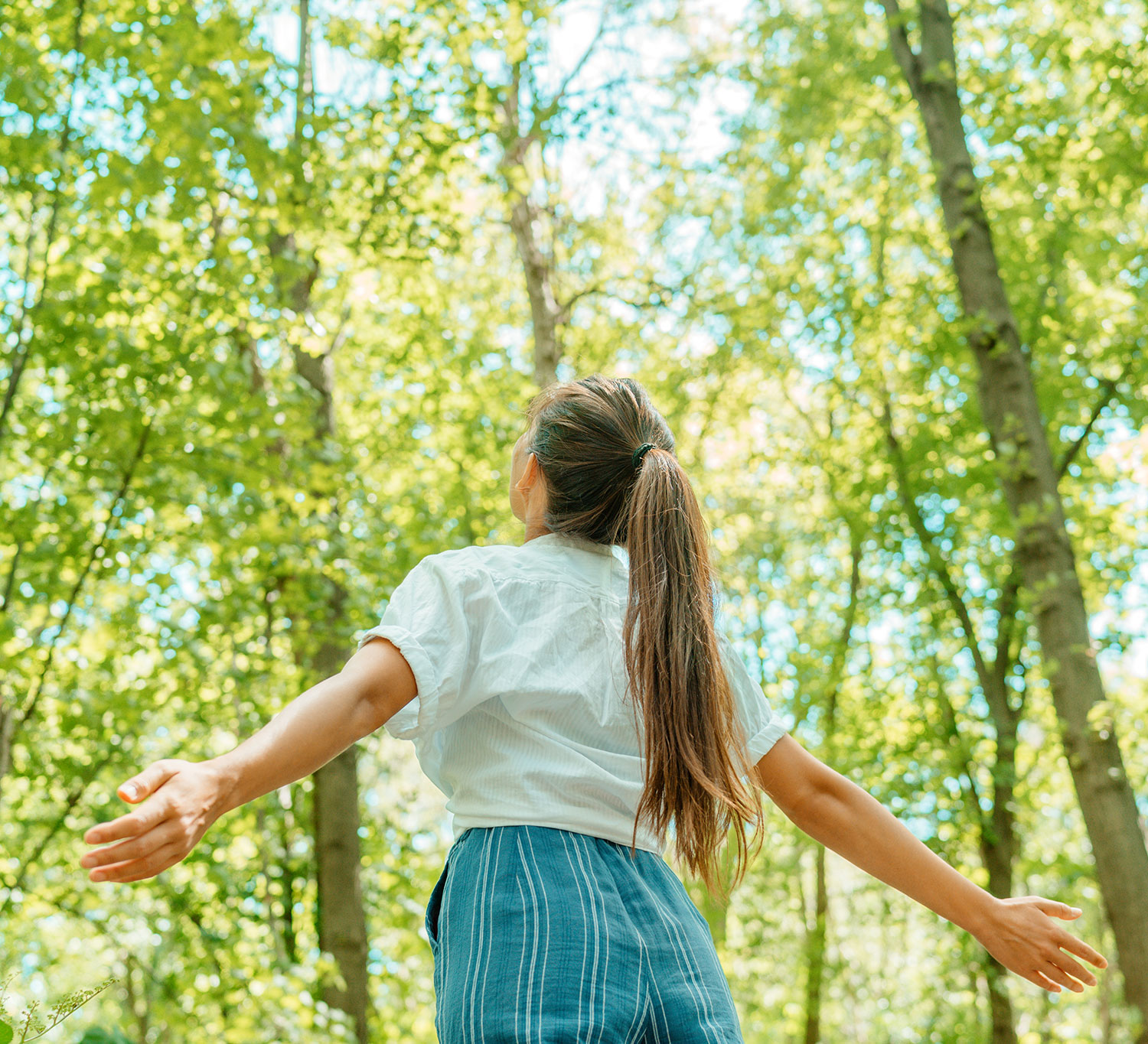 Young woman in the woods looking up with arms open wide happy and pain free from acupuncture treatment for period pain